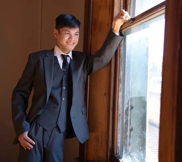 a man in a suit and tie standing in front of a window