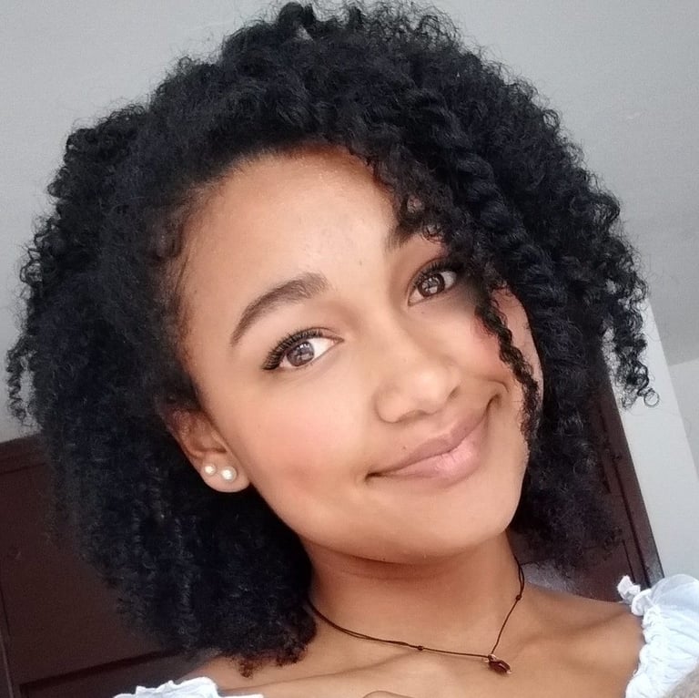Mujer sonriente con cabello negro natural y rizado, peinado en estilo twist out, usando aretes de pe