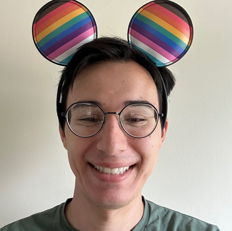 Travel Agent Andrew, wearing rainbow pride mouse ears and smiling.