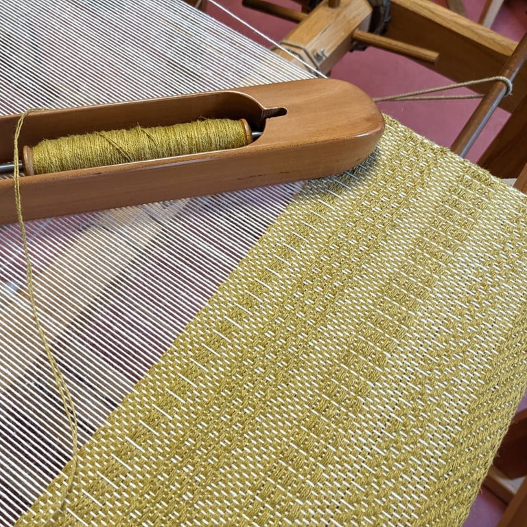 a weaving loom with shuttle and olive green threads on a 4 harness textile in progress
