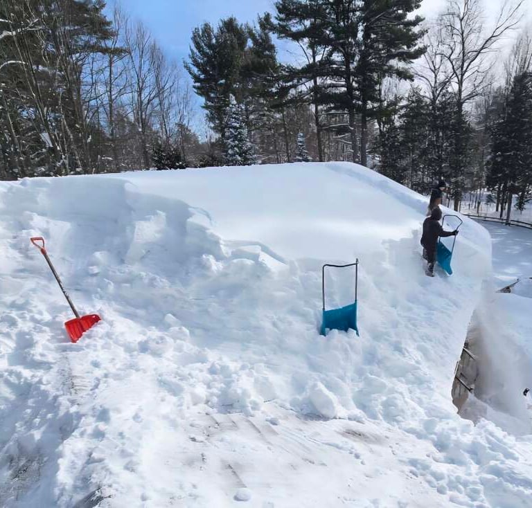 Professional roof snow removal with shovels on a house after a heavy winter storm.