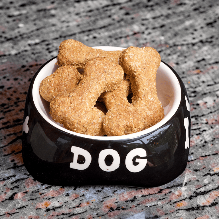 Crunchy bone-shaped homemade dog treats piled in a black ceramic bowl on a granite countertop.