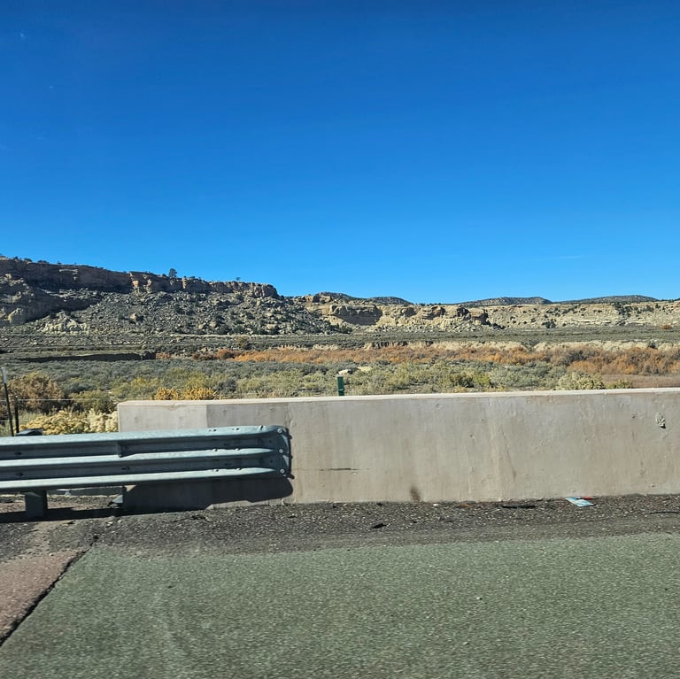 A scenic view of a rocky desert plateau and canyon landscape under a clear blue sky from a highway.
