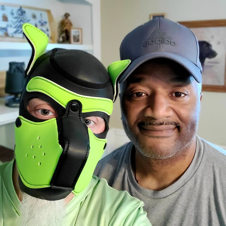 2 men, 1 wearing a pup mask, posing together.