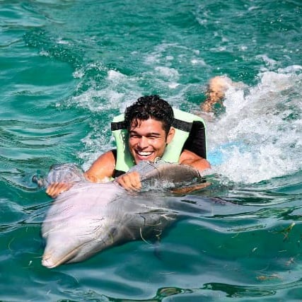 a man in a life jacket is smiling and holding a dolphin dolphines punta cana