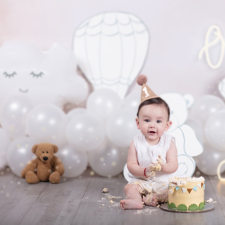 un bebé que acaba de cumplir 1 año de edad, con sombrero de fiesta, un osito de peluche y un pastel