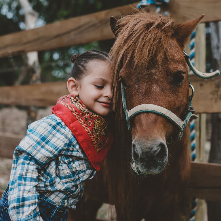 una niña con outfit vaquero abrazando a un pony