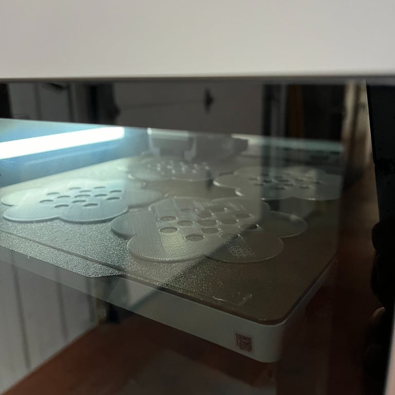 the interior of a 3D printer showing 4 flower frog vase toppers being made from natural PLA plastic