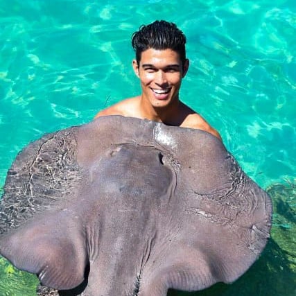 a man in a swimsuit is smiling and holding a stingperk dolphines punta cana