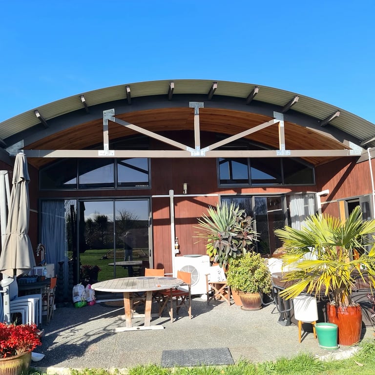 Modern home with tired red exterior, curved roof, and lush patio garden set under a clear Central Hawke’s Bay sky