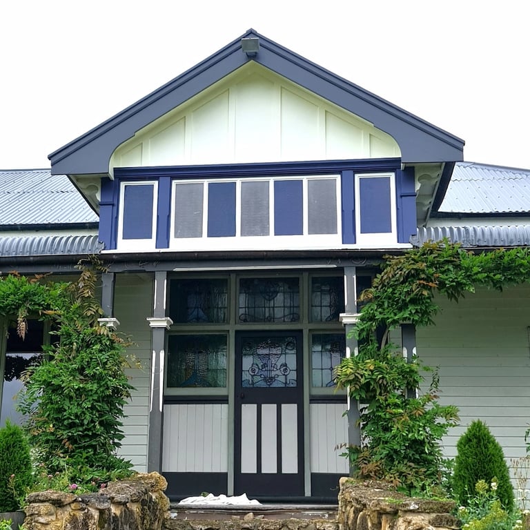 Blue corrugated roof freshly painted, with restored soffits and boards framing a lush, flower-filled entrance