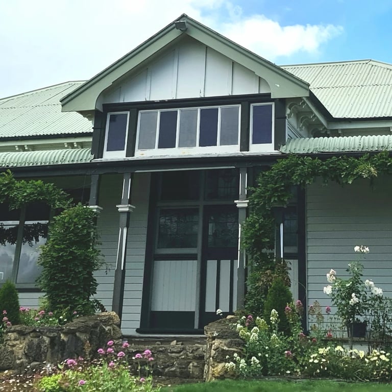 Weathered green corrugated roof with faded soffits and boards, framing a lush garden entrance in Central Hawke’s Bay.