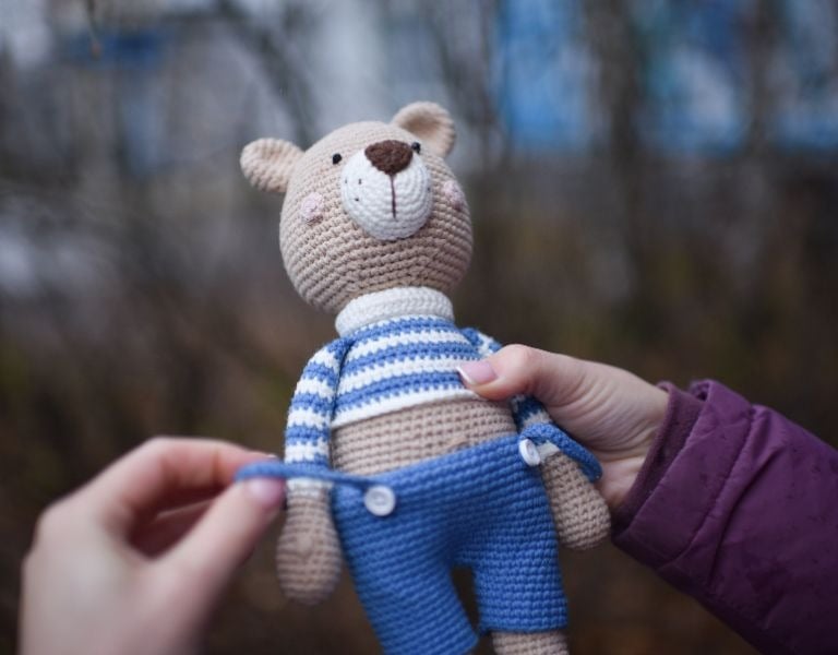 Osito amigurumi tejido a crochet hecho a mano, con suéter a rayas y overol azul.