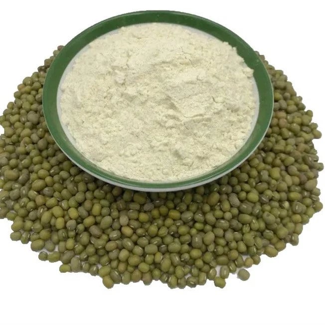 A green bowl of fine white mung bean flour sitting on a pile of raw green mung beans.
