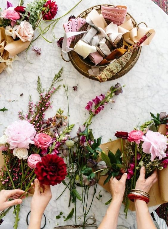 Manos creando una guirnalda floral con rosas y dalias.