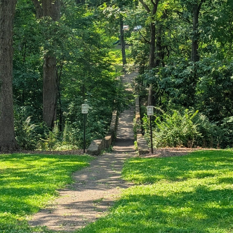 Landscape photo of a bridge in an Iowa park, The bridge is in the center with two lamp posts on either side of the entrnace 