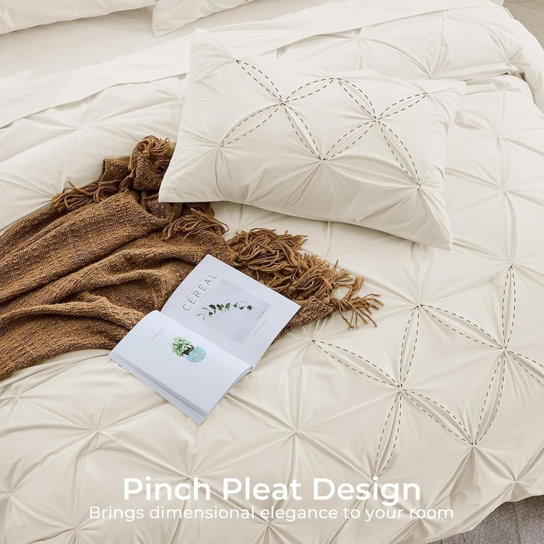 White pinch pleat comforter set with decorative stitching and a brown throw blanket.