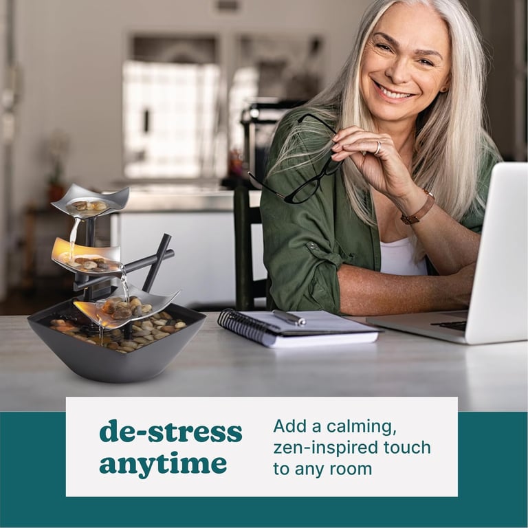 A smiling woman sitting at a desk next to a tiered indoor desktop water fountain for home office relaxation.