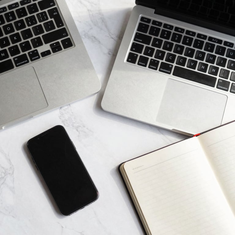 A top-down view of a modern workspace with a laptop, smartphone, and notebook on a white marble surface, illuminated by natural light. Clean, minimal B2B aesthetic.