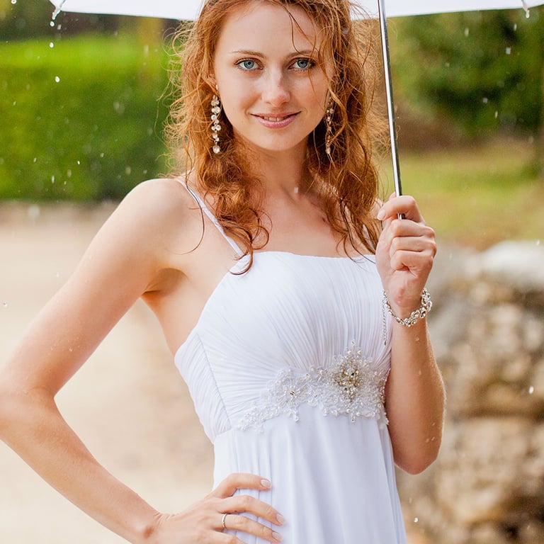 Photo of the bride in the wedding dress holding umbrella under the rain