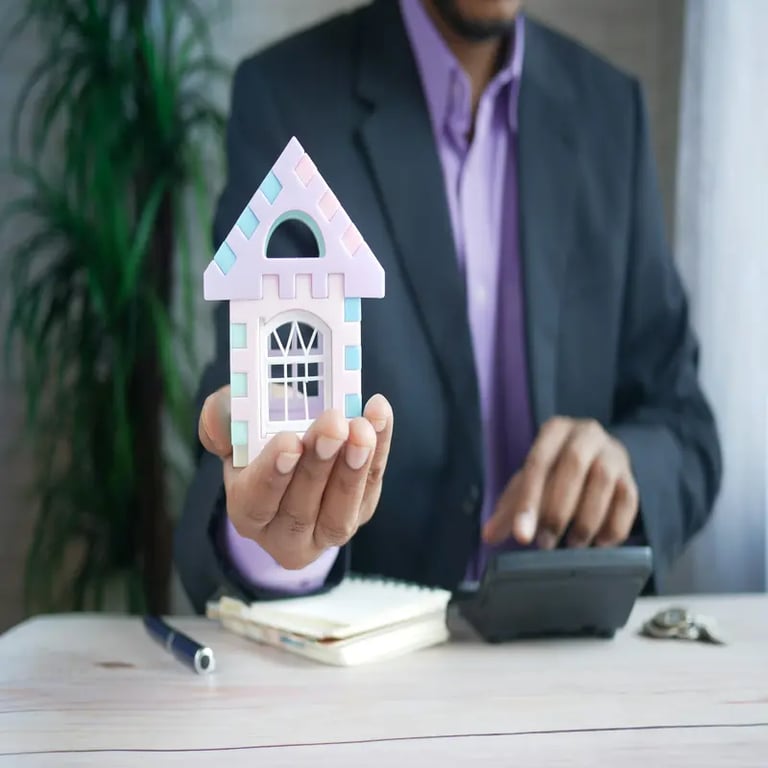 Real estate professional holding a small house model while doing calculations.