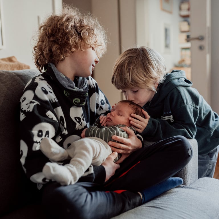 Zwei ältere Brüder kuscheln mit ihrem Baby Bruder