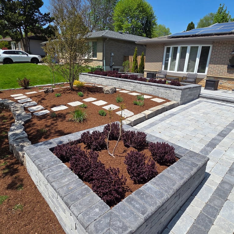 Modern front yard landscaping with interlocking stone pavers, raised garden beds, and mulch.