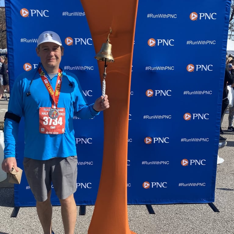 Man wearing a metal and running number, ringing a bell, posing for the camera