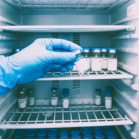 Gloved hand reaching for a vaccine vial stored inside a medical refrigerator.
