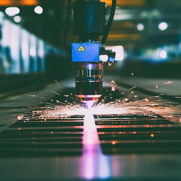 Industrial CNC laser cutting machine processing sheet metal with sparks in a factory.