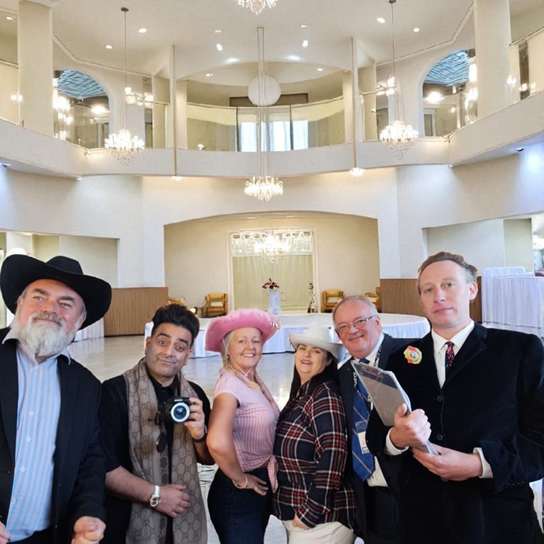 Diverse group of event professionals wearing cowboy hats posing in a grand ballroom with chandeliers.