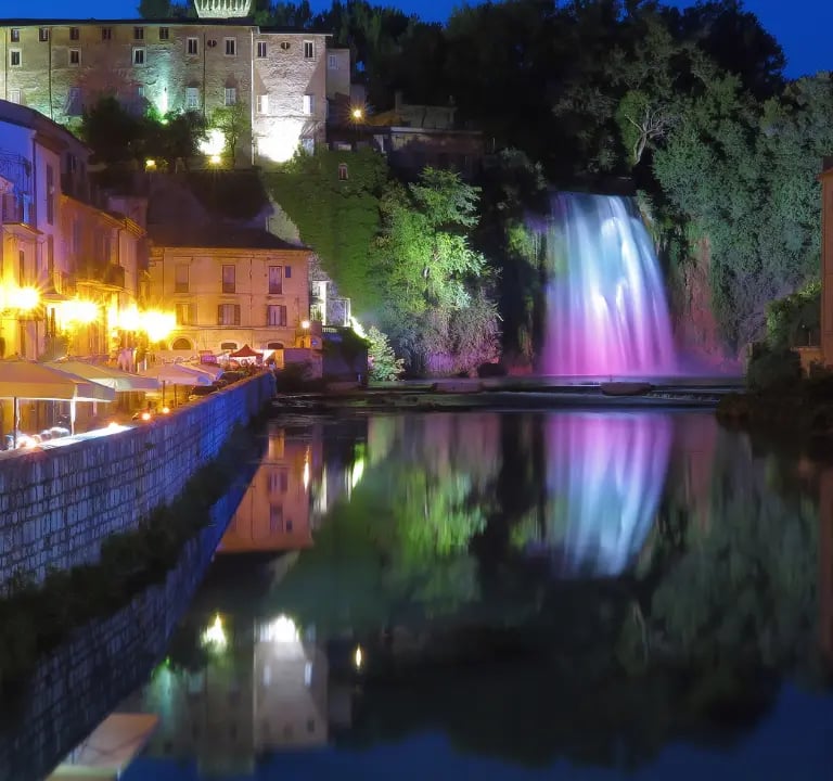 The Great Waterfall of Isola del Liri illuminated at night with colorful lights reflecting on the river