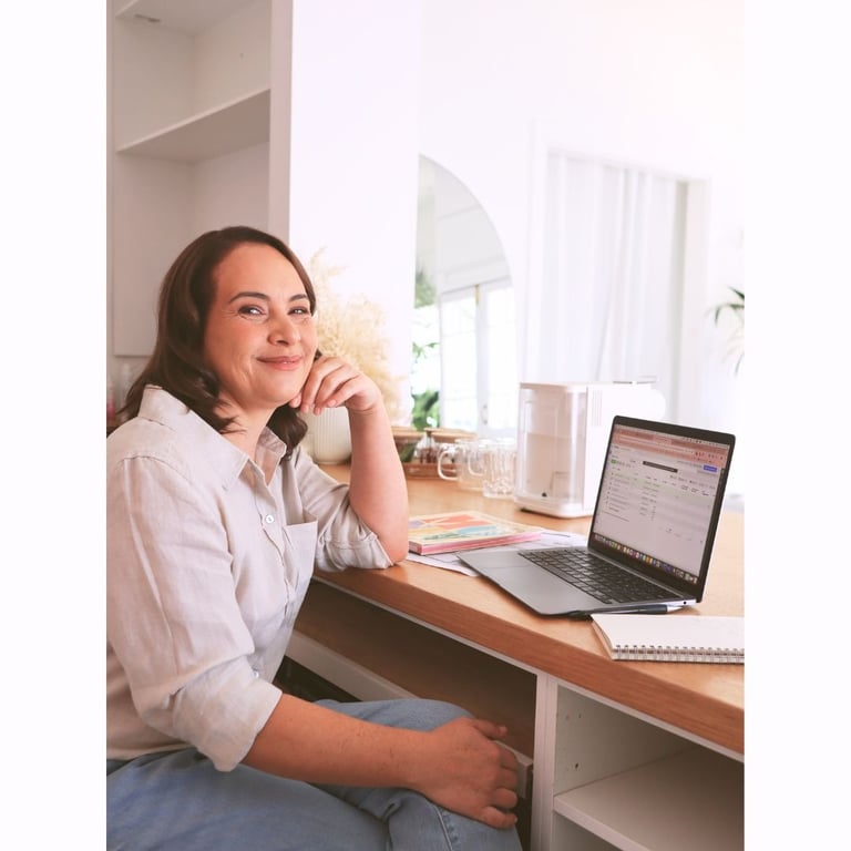 Milly smiling while working on a laptop in a bright, organised home office.