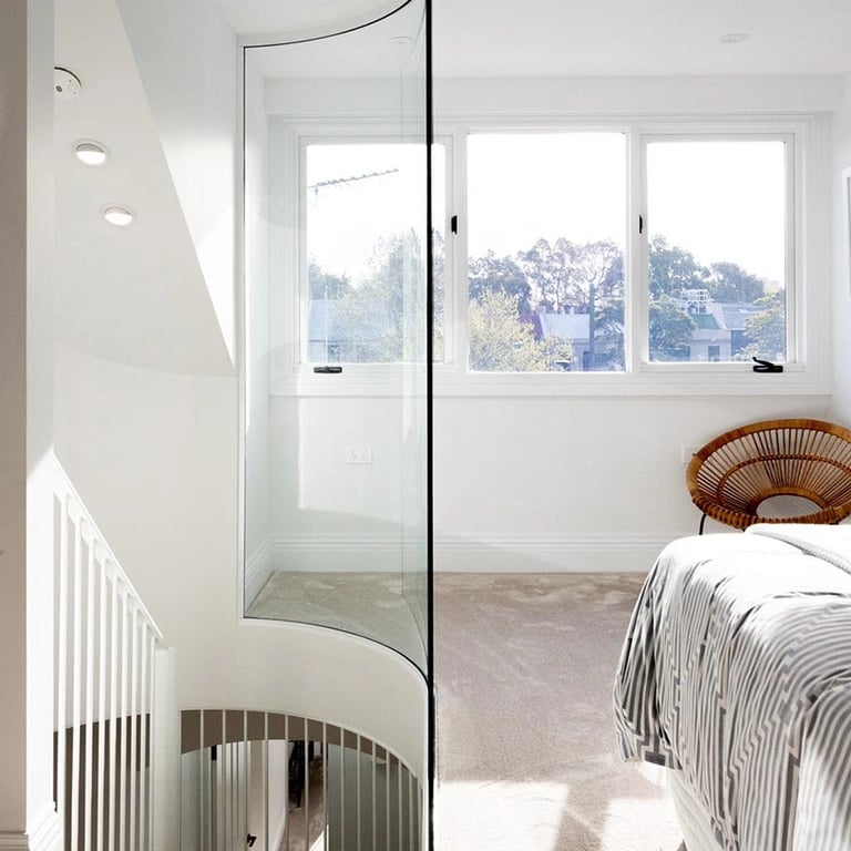 Attic retreat bedroom with curved glass wall, diffused light, and a sense of vertical spaciousness.