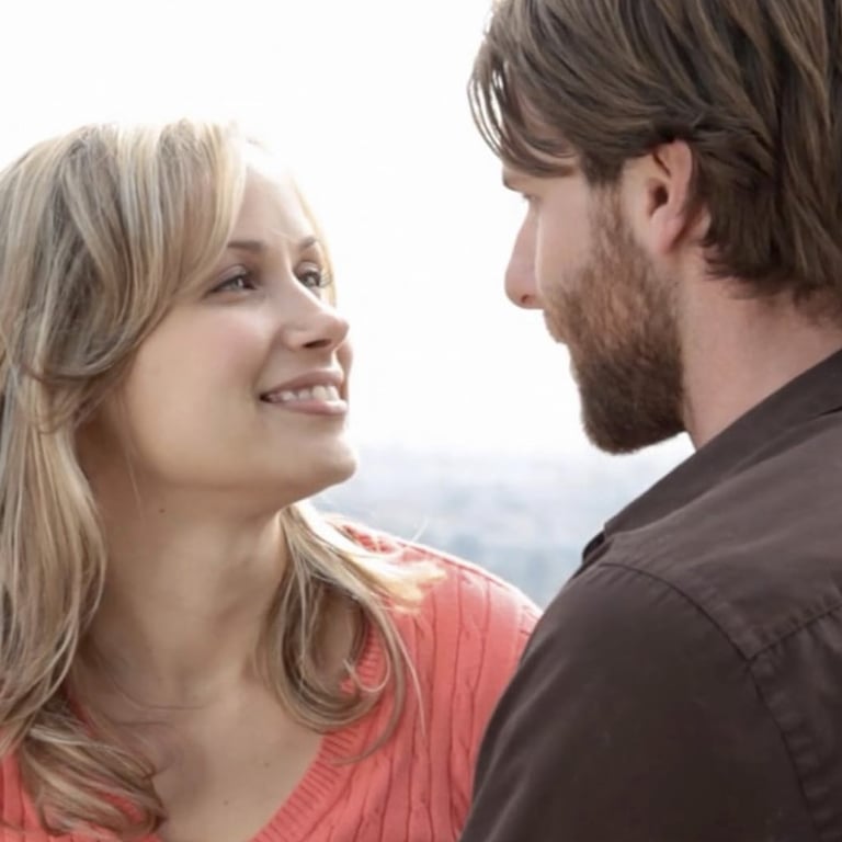 A thirty-something man and woman sit on a balcony looking into each other's eyes