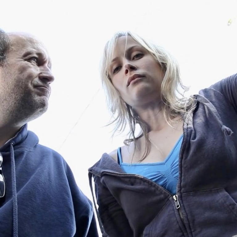 A young blonde woman and a balding middle-aged man peer down into the boot of a car