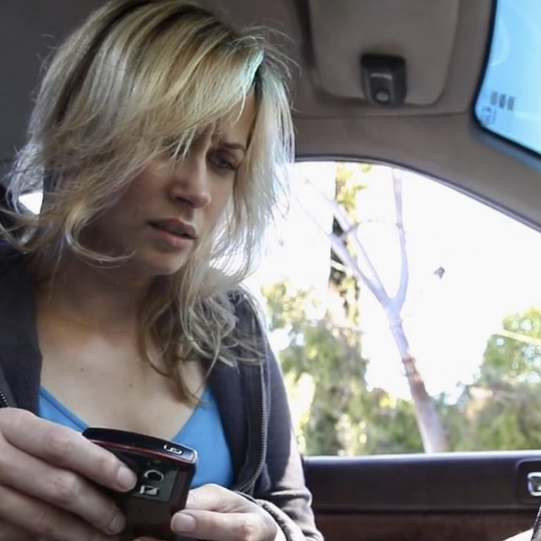 A young woman is sitting in the driver's seat of a stationary car with a mobile phone in her hand