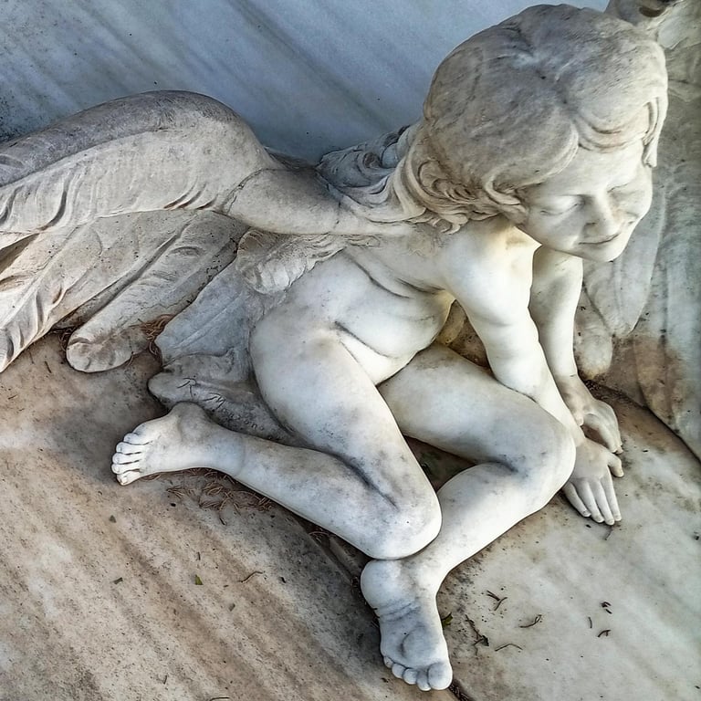 A detailed white marble cherub statue with feathered wings resting on a marble surface.