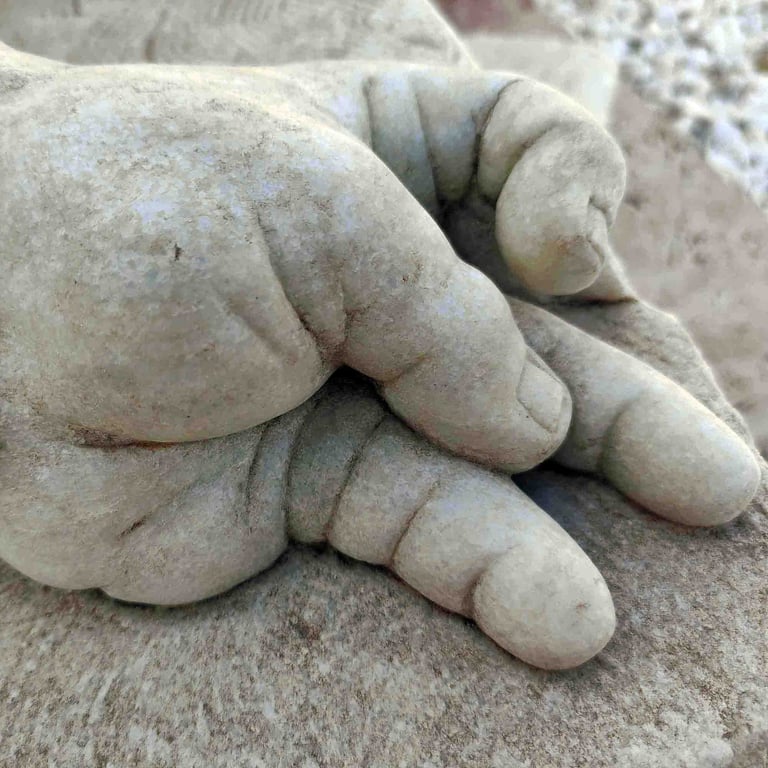 Close-up of a white marble sculpture depicting a chubby baby hand resting on a rock.