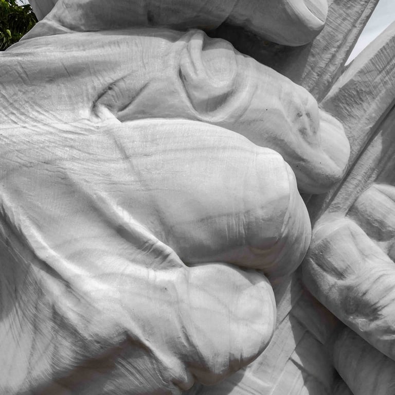 White marble sculpture of large hands weaving a mat with esparto grass on a stone pedestal in a squa