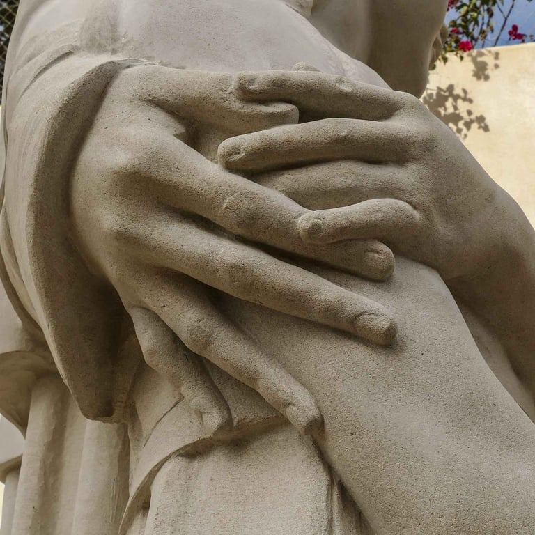 Close-up of stone sculpture showing detailed hands embracing a figure with realistic texture.
