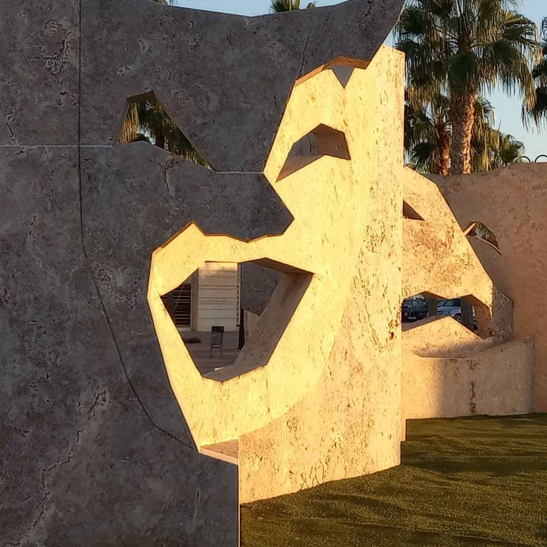 Large stone theater mask sculptures with palm trees in the golden hour sunlight.