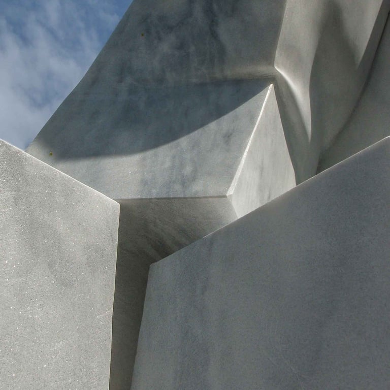 Abstract white marble sculpture with geometric stone shapes and sharp shadows against a blue sky.