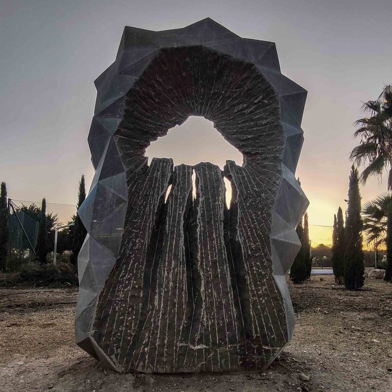Modern sculpture of grey limestone in a park surrounded by trees during sunset