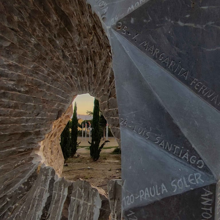 Stone memorial monument with engraved names featuring a carved hole looking out toward trees at sunset.