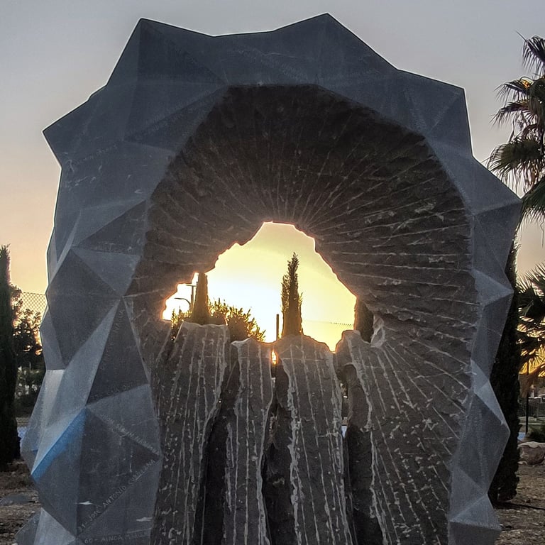 A geometric stone monument framing a golden sunset landscape through a jagged central cutout.