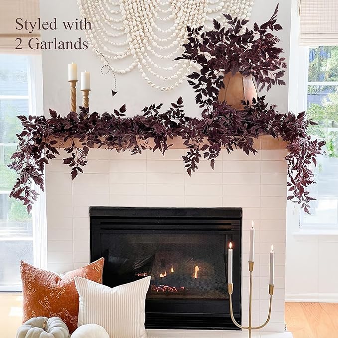 White fireplace mantel styled with two burgundy faux garlands, candles, and fall pillows