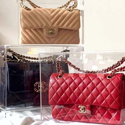 Set of three acrylic display cases holding beige, black, and red handbags.