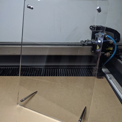 Clear acrylic standee frame with metal standoff mounts on a wooden surface.