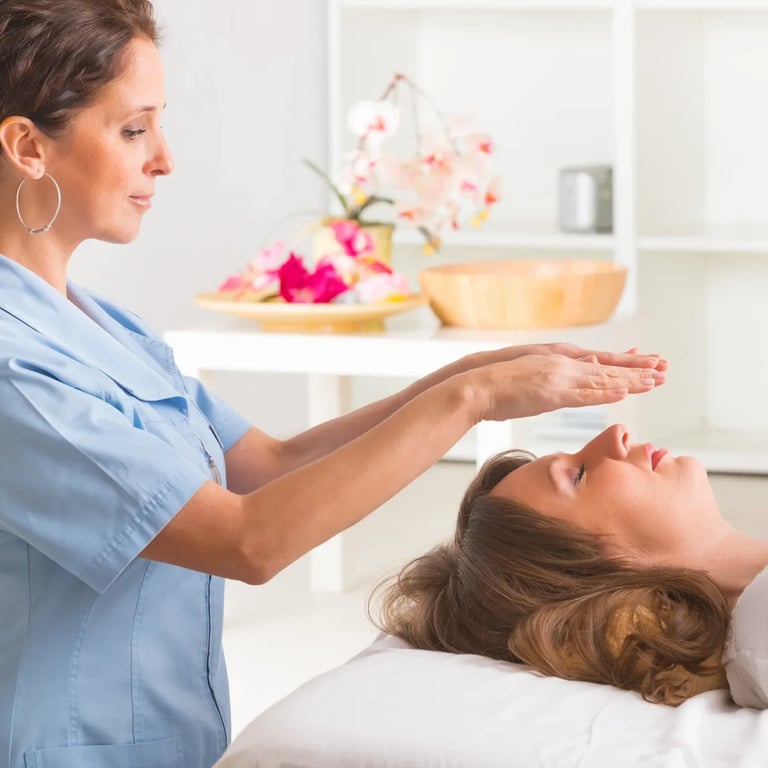 A standing Reiki Practitioner hovers her hands above a client's face who is laying down